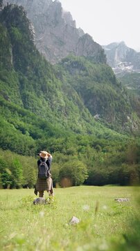 Female hiker taking photos with a professional camera while exploring a scenic forest with mountain views, combining hiking, travel and nature photography.