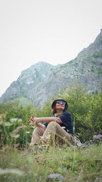 Female hiker relaxing in a blooming mountain meadow and enjoying a breathtaking mountain view during a peaceful hiking adventure in nature.
