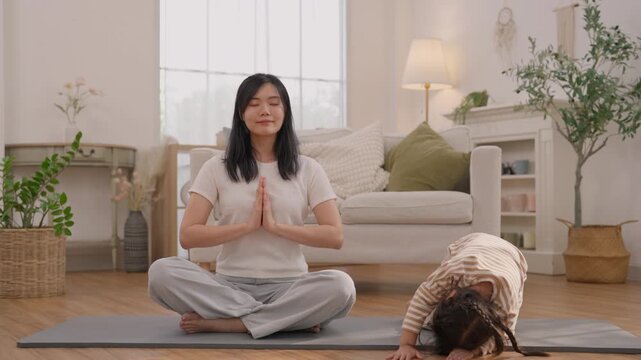 Woman and child meditation yoga exercise on yoga mat in bright living room, calm family wellness living scene with sitting, natural plants, sofa, soft home lighting, peaceful mindful practice