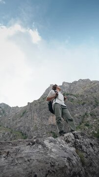 Young female hiker with a backpack standing on a rock and enjoying a breathtaking mountain view, capturing hiking, adventure, freedom and exploration in nature.