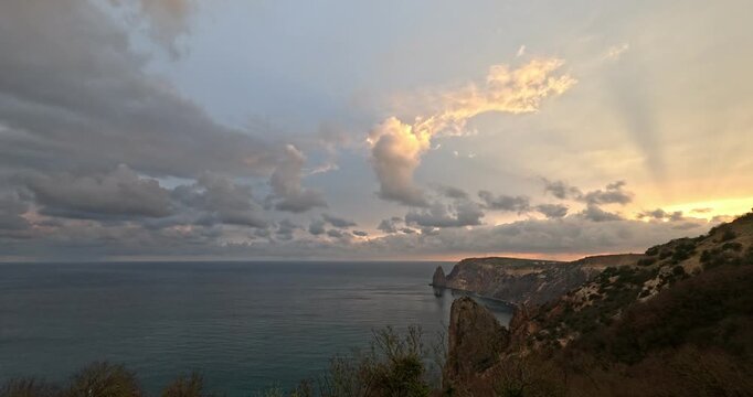 Dramatic cloud formations drift above the dark coastal waters at sunset near Fiolent cliffs. Static wide angle shot.