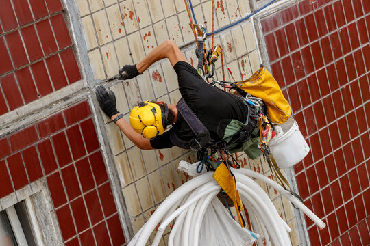 Industrial climber cleaning a seam on a tiled building facade at height.