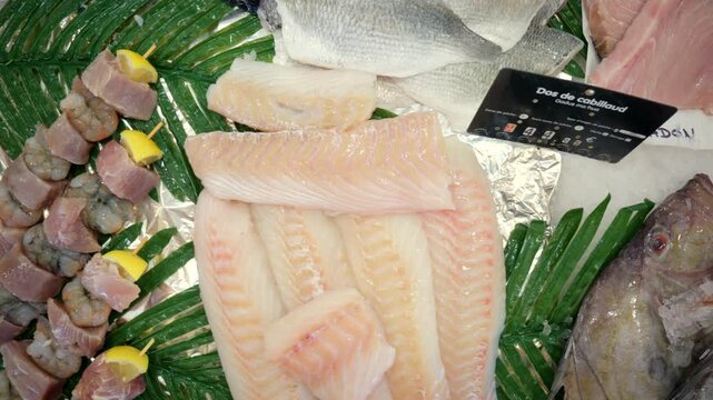 Displaying various raw seafood products including cod fillets and whole fish, arranged on ice at a market stall