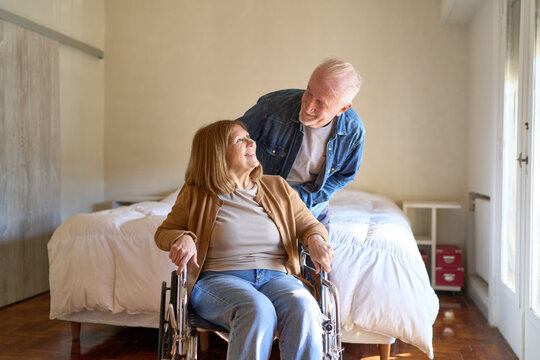 Elderly couple with home healthcare and senior care, man assisting woman in wheelchair in a bright living room