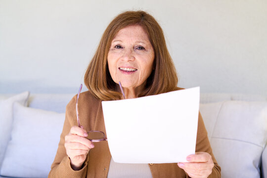 Senior woman reading documents at home, elderly independence and self-care, healthy aging and wellness in a bright living room