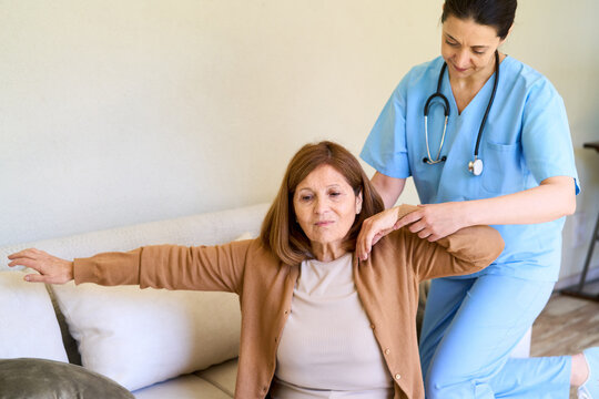 Home healthcare and senior physical therapy, nurse assisting elderly woman with arm exercises in a bright living room