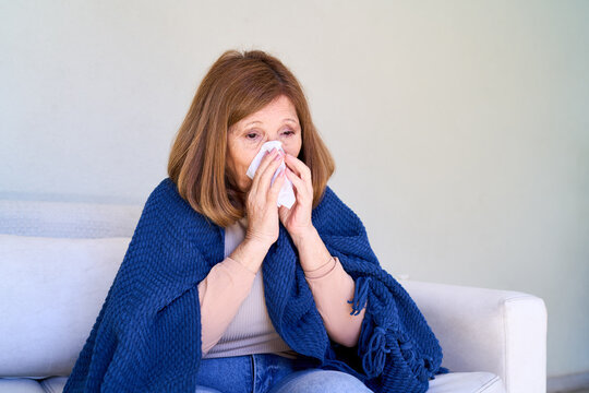 Elderly woman with cold or flu symptoms, blowing nose with tissue, home healthcare and senior wellness