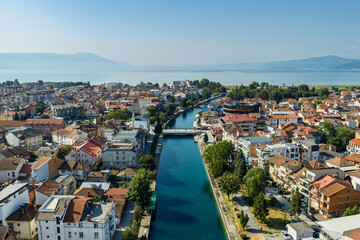 Fototapeta premium Aerial drone view of Struga in North Macedonia with Black Drin River flowing into crystal clear Lake Ohrid, boats, sunny summer landscape, waterfront buildings and scenic city panorama