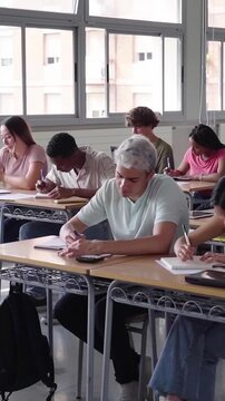 Diverse large group of students in a bright classroom studying. The scene highlights education, learning and collaboration. Vertical video with copy space.