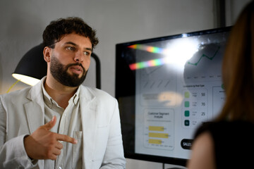 Fototapeta premium Businessman discusses sales data with colleague in modern office setting during meeting