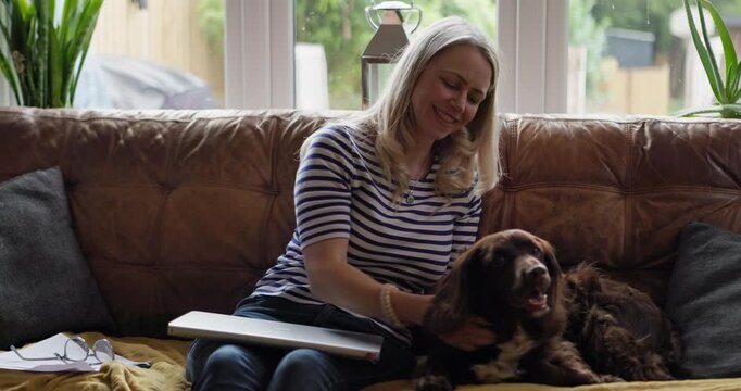 Woman, care and kiss dog on sofa for smile on face for love, remote work and relax in living room. Person, pet and animal with stroke, play and happy with laptop, portrait and lounge couch in home