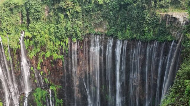 Vertical aerial drone view of Tumpak Sewu Waterfall in Java, Indonesia surrounded by lush green tropical rainforest and steep rocky cliffs