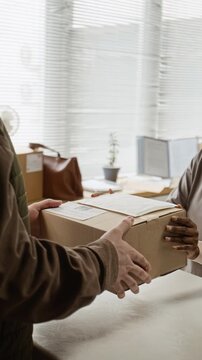 Vertical video of African American female worker handing cardboard box to customer and typing on laptop. Clip is perfect for small business shipping and e-commerce logistics promos