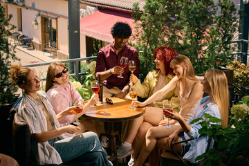 Naklejka premium Large group of friends relaxing with wine on outdoor terrace. Concept of shared experiences, group connection, weekend gatherings, hospitality and wine lifestyle marketing.