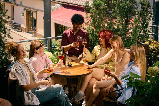 Large group of friends relaxing with wine on outdoor terrace. Concept of shared experiences, group connection, weekend gatherings, hospitality and wine lifestyle marketing.