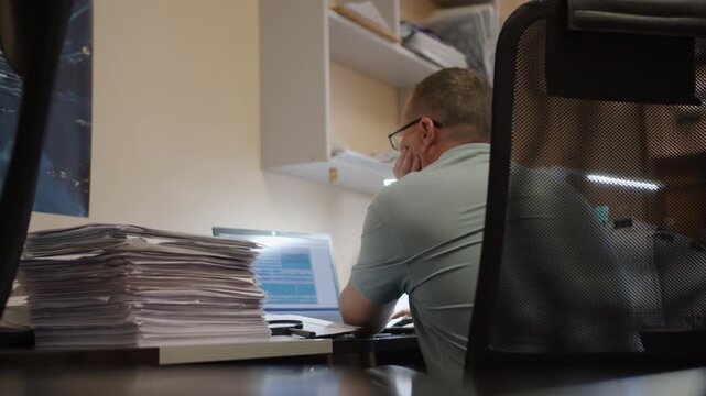 Office Worker Using Laptop Beside Stack of Documents