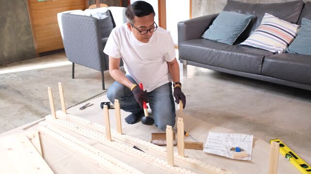 Focused man using tool for wood furniture assembly at home, building wooden frame on living room floor