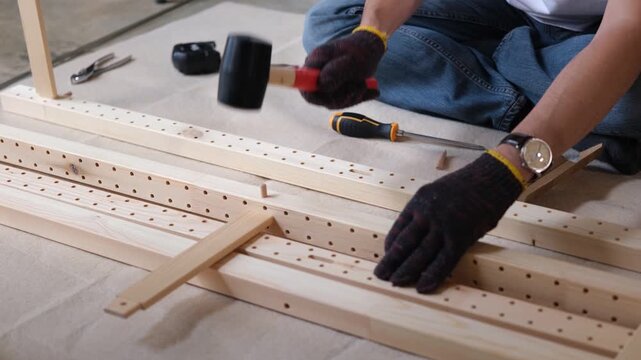 Furniture assembly wood plank mallet hand craft on floor, gloved worker builds flat pack shelf frame for home interior
