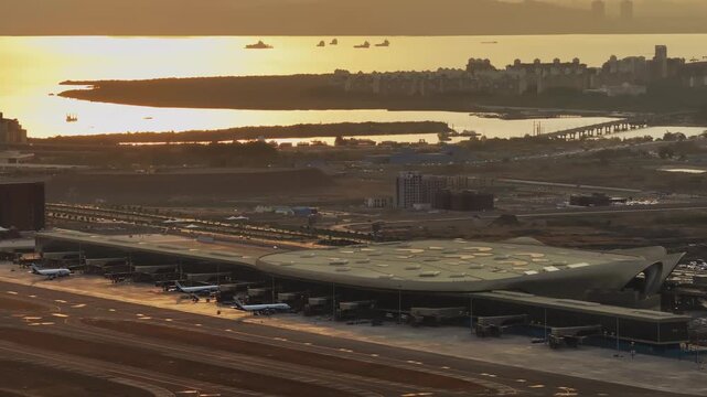 Aerial view of Navi Mumbai International Airport during sunset, showcasing the modern terminal, runways, surrounding waterways, and urban landscape of Navi Mumbai.