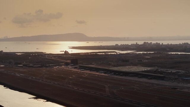 Aerial view of Navi Mumbai International Airport during sunset, showcasing the modern terminal, runways, surrounding waterways, and urban landscape of Navi Mumbai.