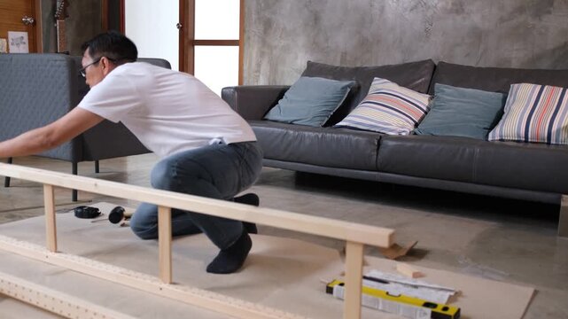 Furniture assembly man builds wood frame sofa in living room with tool level focused repair posture home