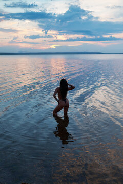 A sensual girl on the beach during a seaside vacation: the tanned back of a beautiful athletic woman in a black bikini. Summer vacation. Phuket, Thailand. Rear view. Sunset.