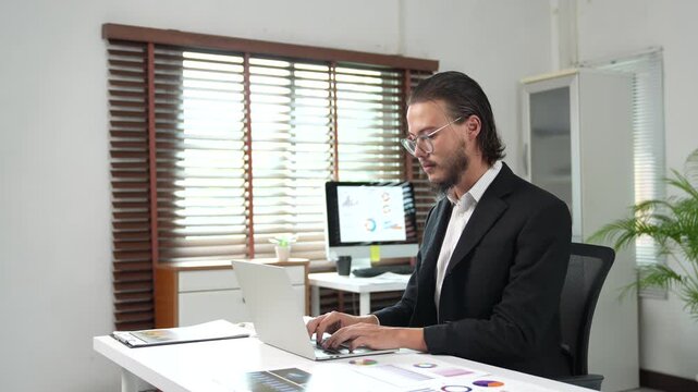 Professional businessman typing on laptop computer analyzing financial data, graphs and charts for corporate strategy, marketing research, and business development in an office