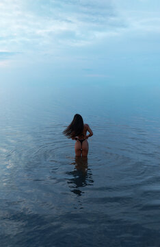 A sensual girl on the beach during a seaside vacation: the tanned back of a beautiful athletic woman in a black bikini. Summer vacation. Phuket, Thailand. Rear view. Sunset.