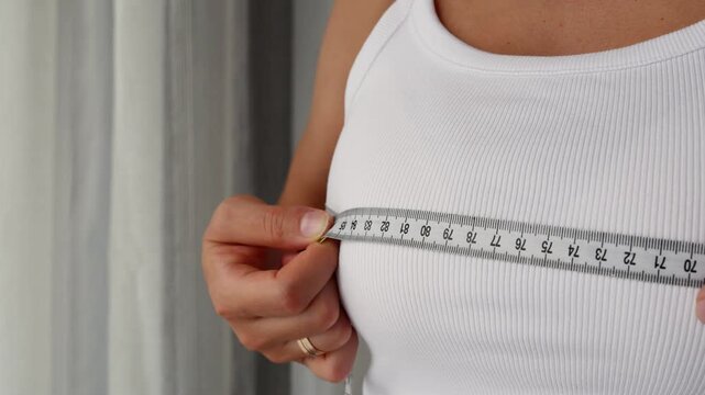 Close-up of woman checking bust measurement with tape for fitness and body transformation