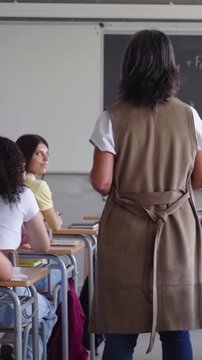 High school students concentrated during exam with teacher watching them, walking around. Vertical footage with copy space.