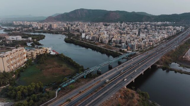 Aerial view of Navi Mumbai showcasing modern highways, bridges, urban development, water bodies, and scenic hills in the background. The image highlights the blend of modern infrastructure.