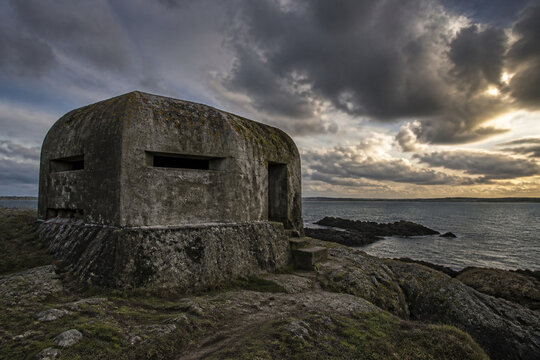 Weathered concrete bunker on a rocky coastline covered in moss.