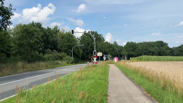 Rural road and pedestrian bicycle path leading toward railway level crossing between agricultural fields