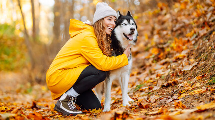 Woman in bright raincoat is having fun with her dog in an autumn park. Young woman enjoys autumn in park, walking husky outdoors. Concept of friendship, animals, and walking. Lifestyle. © maxbelchenko