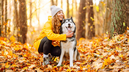Woman in bright raincoat is having fun with her dog in an autumn park. Young woman enjoys autumn in park, walking husky outdoors. Concept of friendship, animals, and walking. Lifestyle. © maxbelchenko