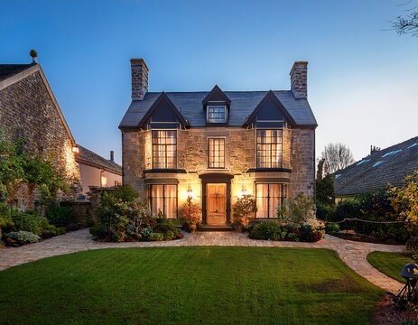 large stone townhouse with lit windows and landscaped front garden