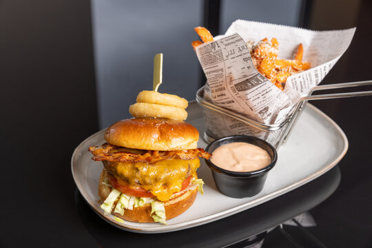 Gourmet cheeseburger with bacon, onion rings, dipping sauce, and seasoned fries in a wire basket