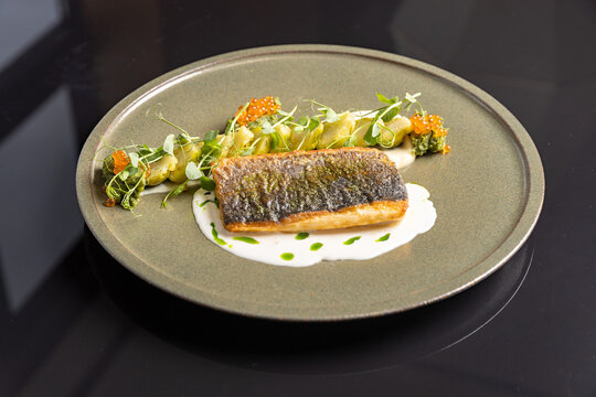 Pan fried sea bass fillet with crispy skin, creamy sauce, salmon caviar, and fresh herbs on a plate