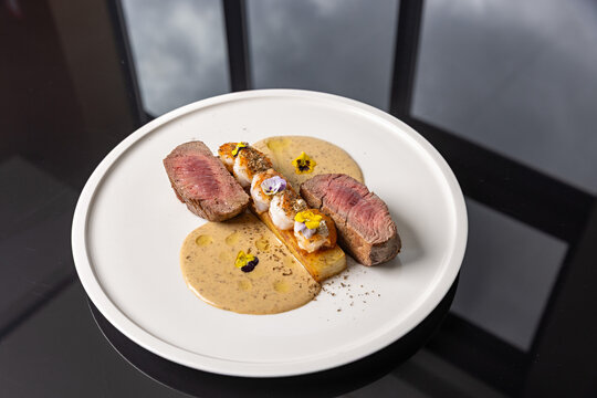 Gourmet surf and turf steak with grilled prawns, potato terrine, creamy sauce, and edible flowers