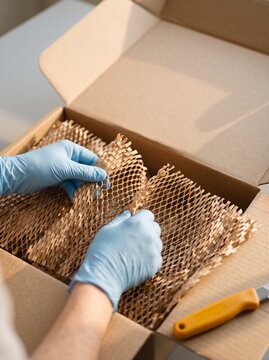 Hands in blue protective gloves unpacking sustainable honeycomb paper wrapping inside a cardboard shipping box