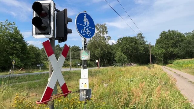 Railway level crossing with signal, crossbuck and pedestrian bicycle path beside rural road