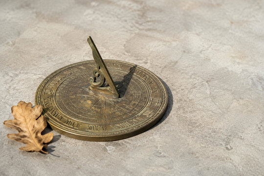 Antique bronze sundial with dried oak leaf on grey stone, time and history concept