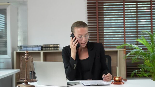 Professional lawyer talking on the phone with a client while reviewing legal documents and offering legal advice and consultation from her modern law firm office