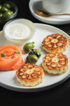 Savory Syrniki with Smoked Salmon, Olives and Sour Cream on White Plate