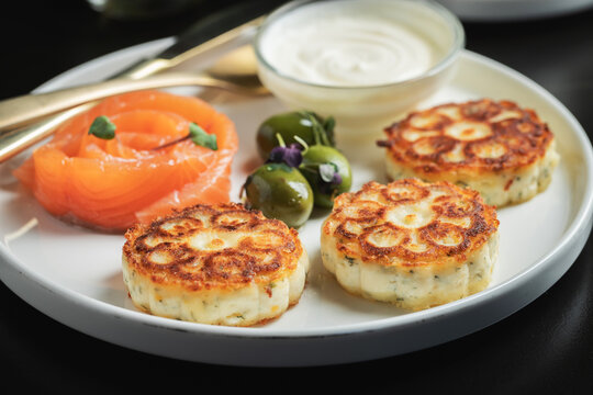Savory Syrniki with Smoked Salmon, Olives and Sour Cream on White Plate