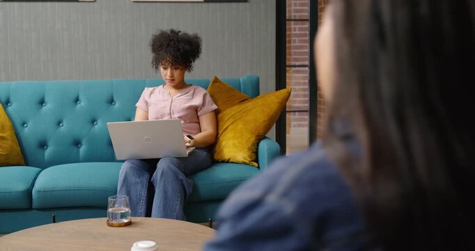 Female coworkers passing as woman glancing, resuming typing to continue work on laptop in office