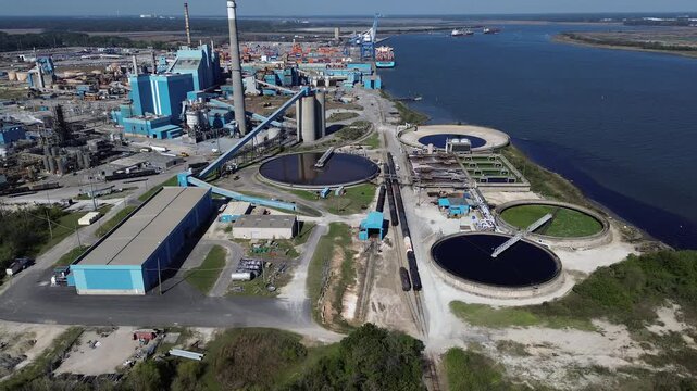 Large wastewater clarifiers operate beside South Carolina Cooper River docks near Charleston Farms. Ground level rail lines transport chemical cargo across North Charleston
