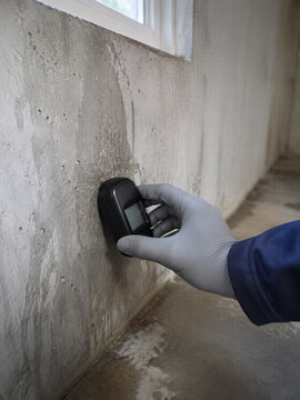 Gloved property inspector measuring moisture damage on a stained concrete wall. Building inspection and water leak assessment for insurance claim and renovation planning.