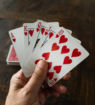Hand Holding Royal Flush in Hearts Over Dark Wooden Table