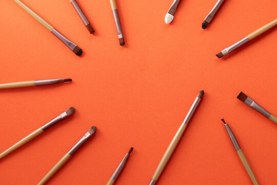 Various sizes and shapes of cosmetic makeup brushes on a bright orange background.